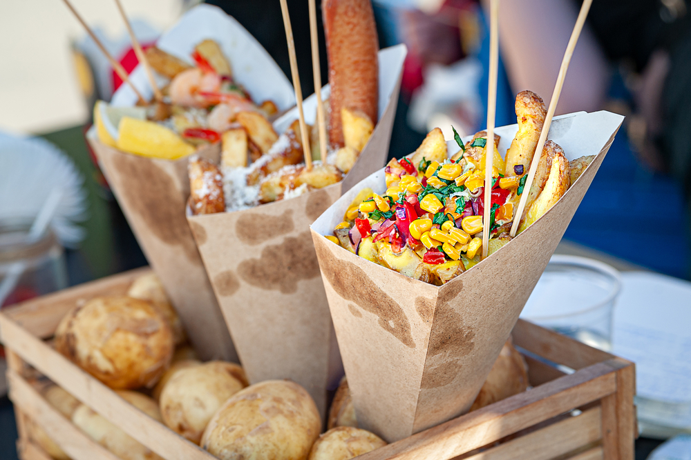 Street food. French fries with vegetables folded into a paper bag on a stand. a close up of a tray of food