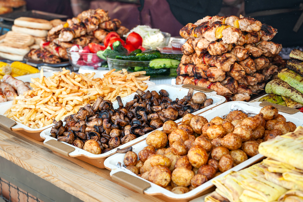 Street food. A lot of grilled meat, grilled mushrooms and grilled vegetables on the window of a street diner. a bunch of food on a table