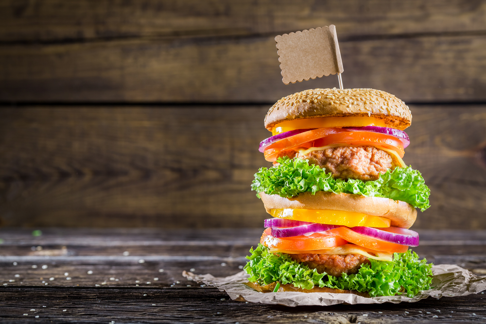 Tasty and big double-decker burger a close up of a sandwich sitting on top of a wooden table