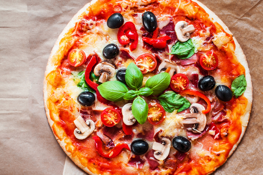 Hot pizza slice with mushrooms, tomatoes, cheese and basil leaf, flat lay a pizza sitting on top of a wooden table