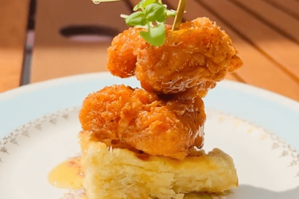 Fried chicken skewered on bread with greens on a plate.