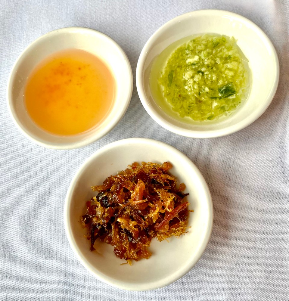 Three small bowls with sauces and condiments on a white tablecloth.