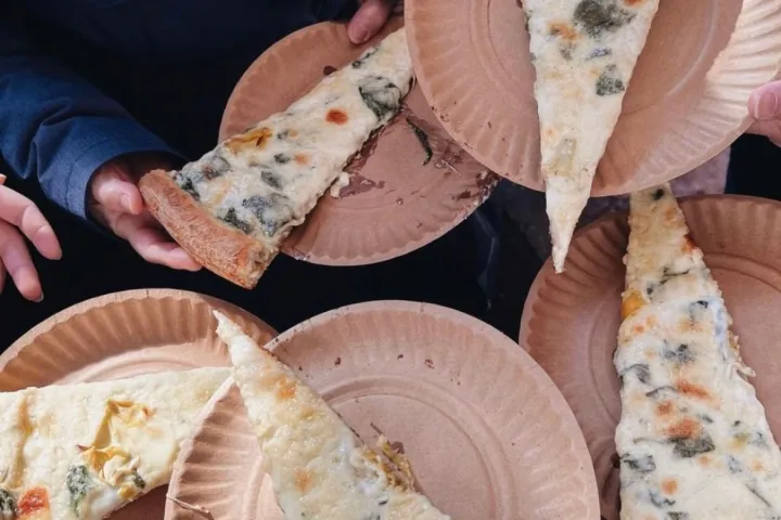 a person holding a slice of pizza on a paper plate
