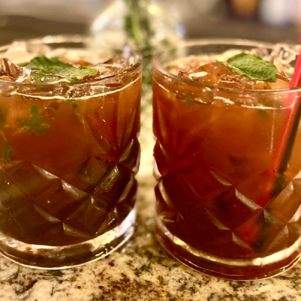 Two iced drinks with mint leaves in patterned glasses on a countertop.