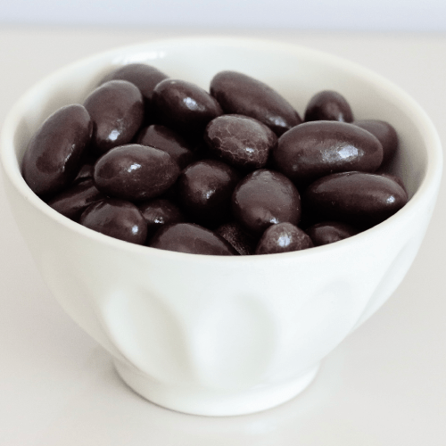 White bowl filled with shiny, dark chocolate-covered almonds.