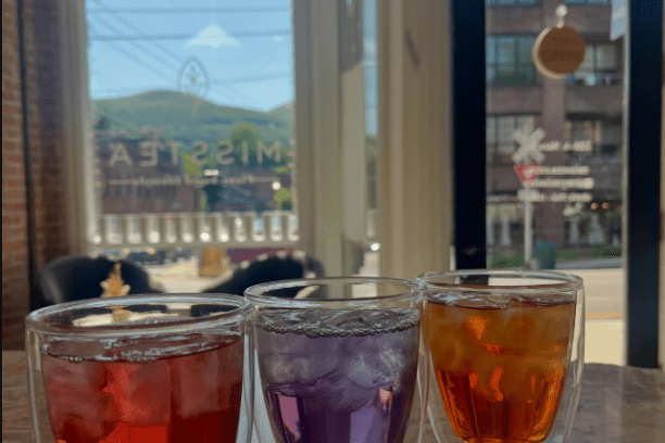 Three colored drinks in double-walled glasses on a stone surface near a window.