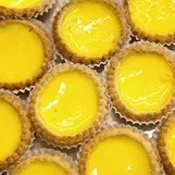 Close-up of multiple yellow egg tarts in pastry shells placed together.