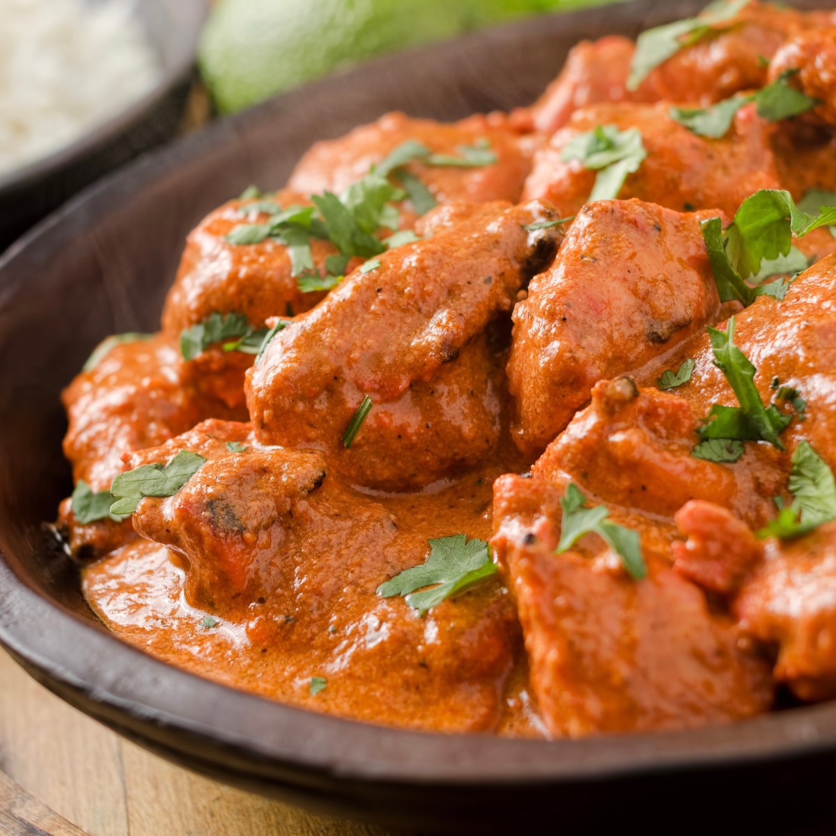 Bowl of creamy orange curry with herbs, next to a side of rice.