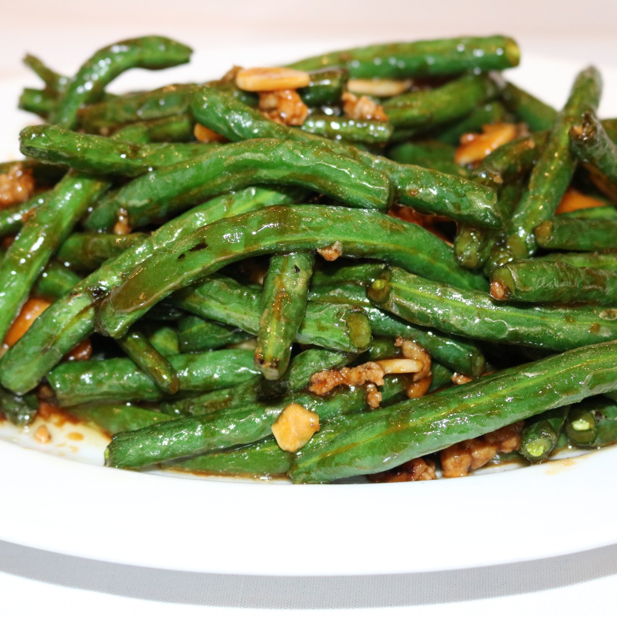 Plate of sautéed green beans with garlic and sauce.